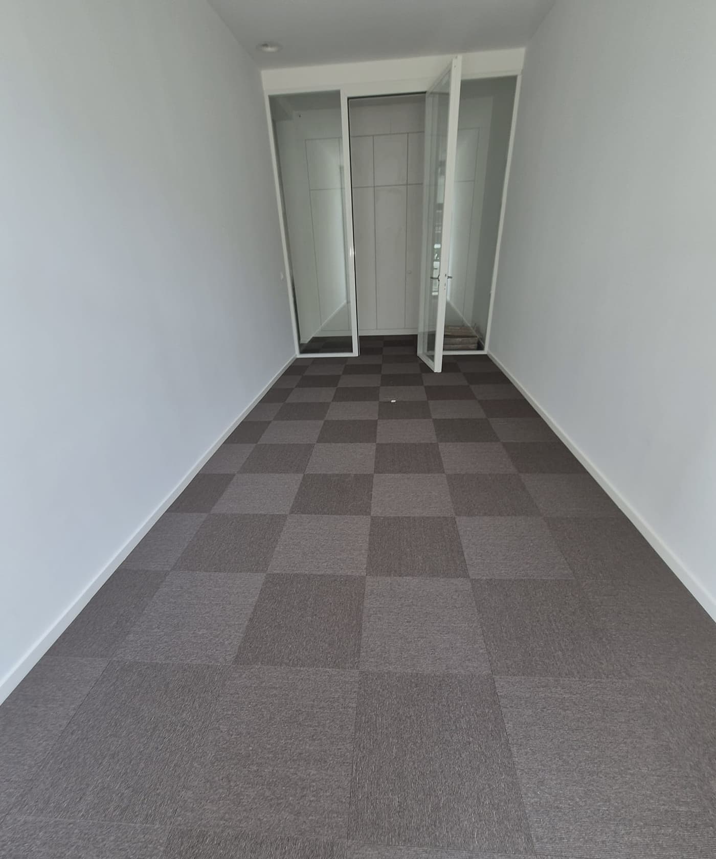 Couloir en dalles de moquette posées en damier, deux tons de gris